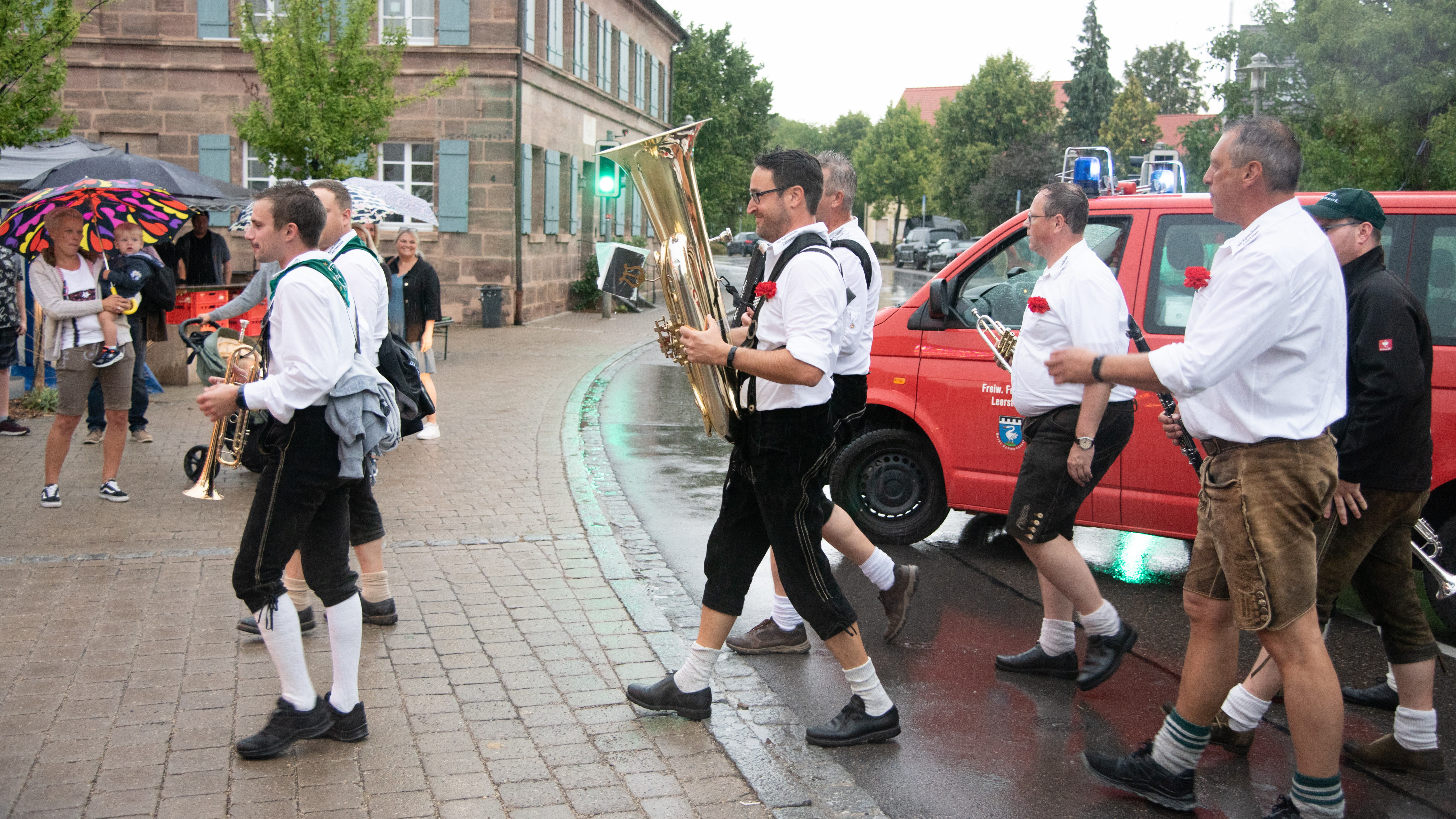  Männliche Mitglieder einer Blaskapelle, in Tracht gekleidet, gehen über die Straße. 