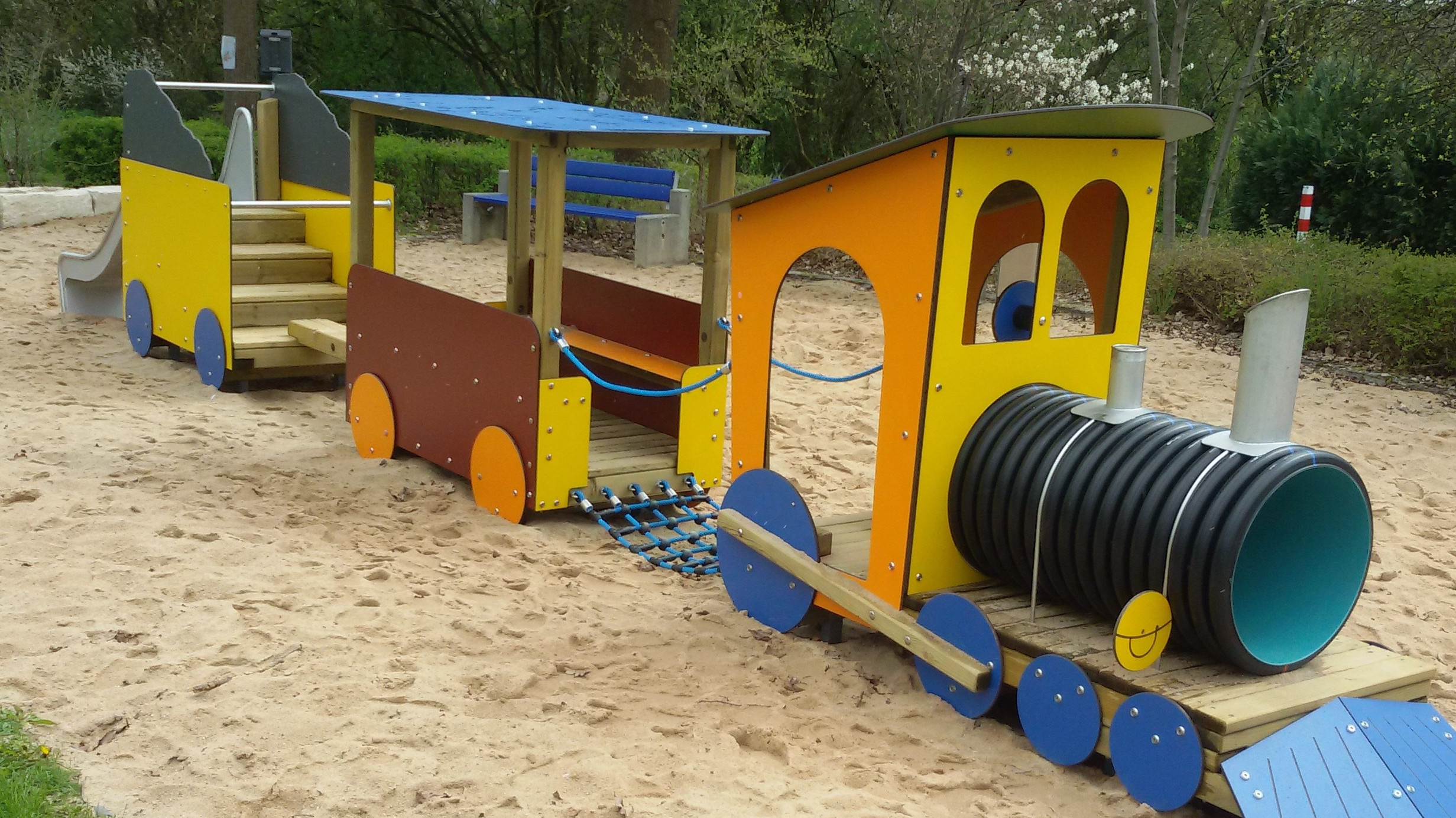  Ein großes Spielgerät in Form eines Zuges steht in einem großen Sandkasten. 